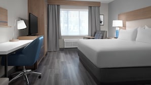 A hotel room with a bed, desk, chair, television, and a window with curtains.