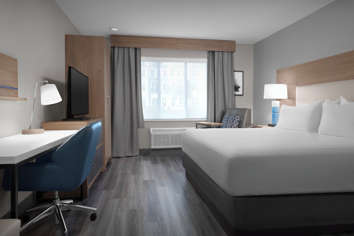 A hotel room with a bed, desk, chair, television, and a window with curtains.