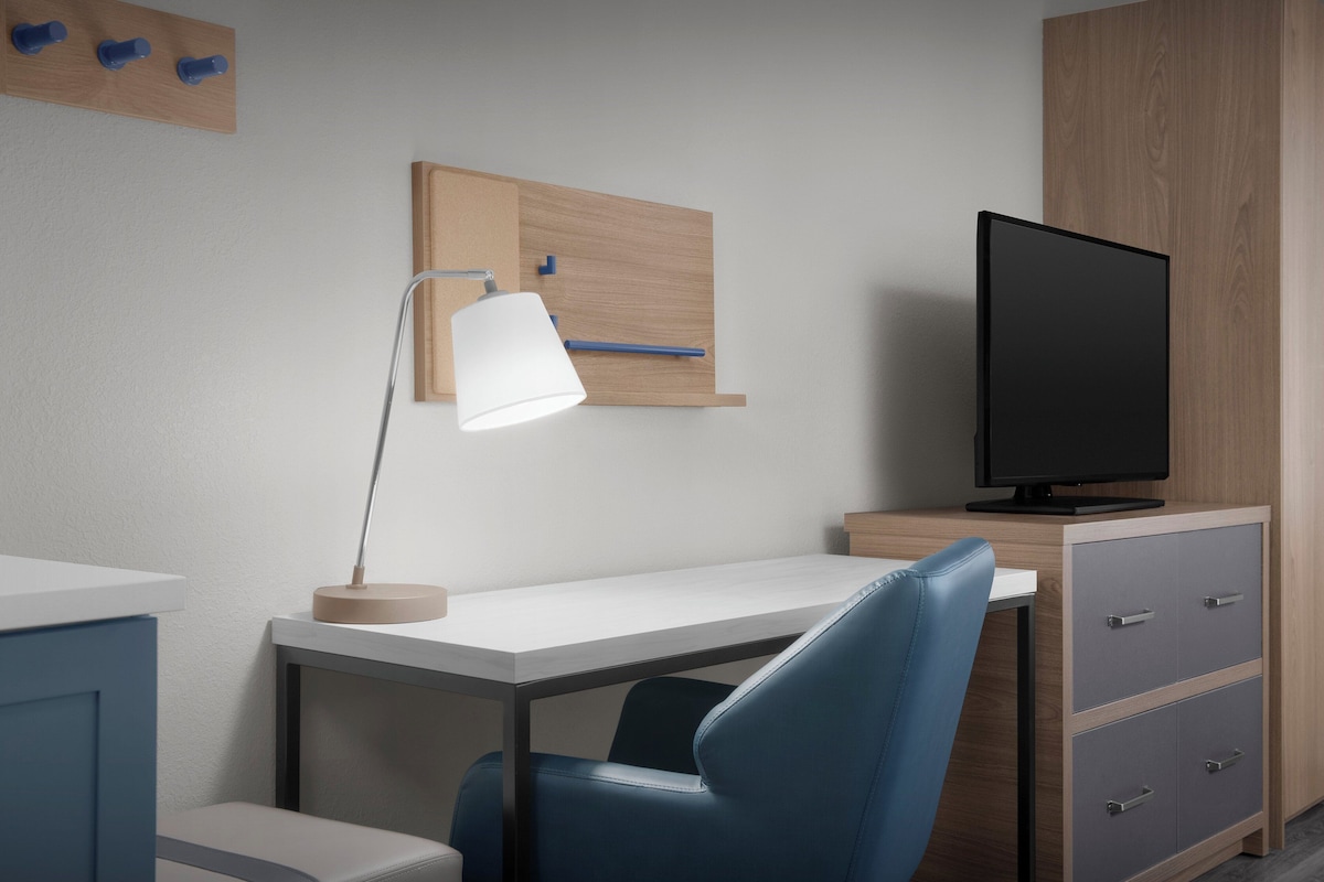A modern hotel room with a desk, a chair, a television, and a cabinet.