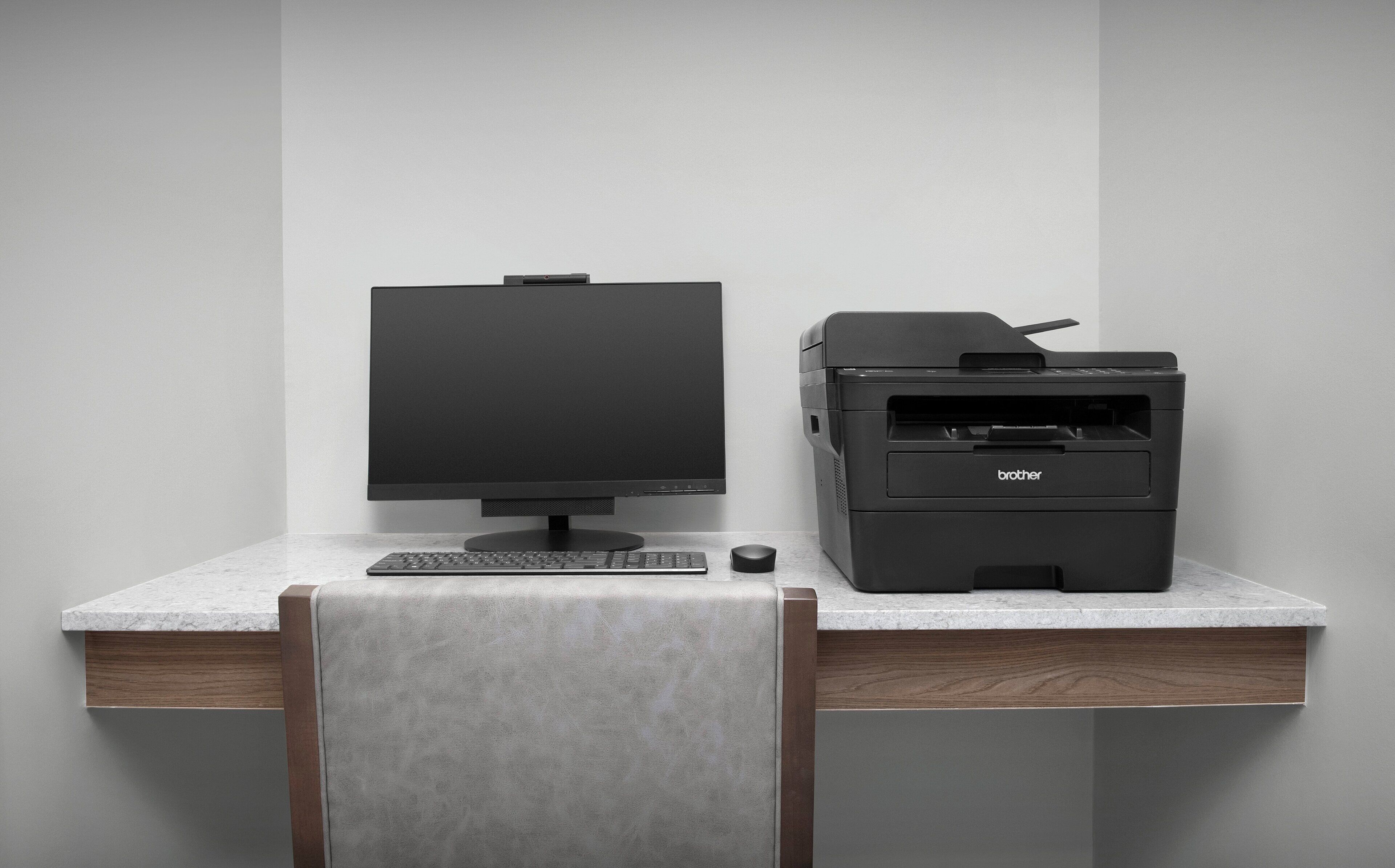 Un bureau moderne équipé d’un ordinateur de bureau et d’une imprimante Brother, le tout posé sur un comptoir en marbre.