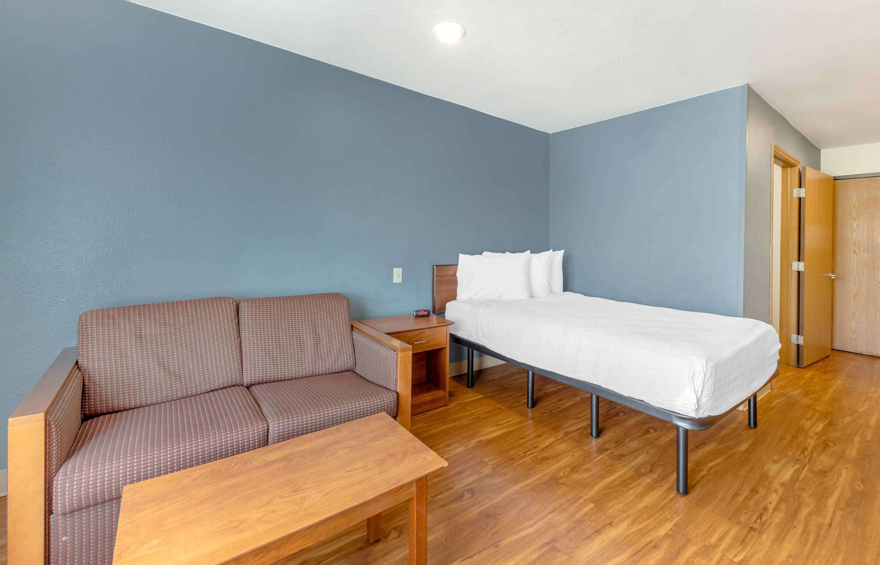 A compact room with a single bed, a sofa, a small table, and a wooden wardrobe.