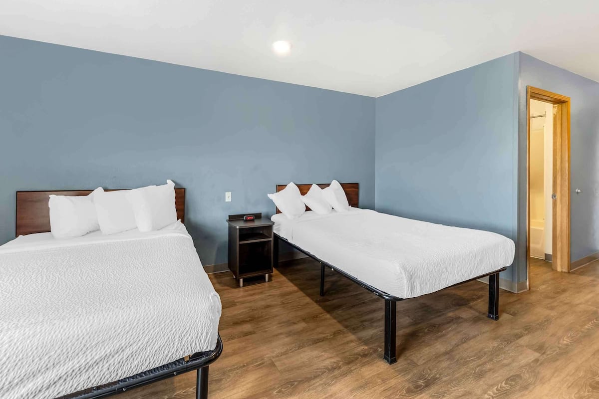 Habitación de hotel con dos camas, una mesita de noche y suelo de madera.