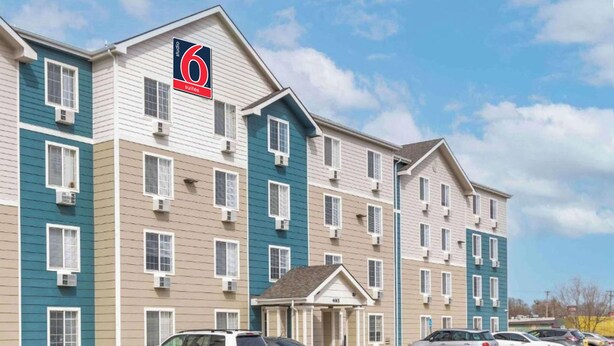 A multi-story hotel with a sign indicating 6 suites, a parking lot with several cars, and a clear sky. - Studio 6 Extended Stay Wichita South KS (Wichita)