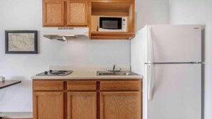 A compact kitchen with wooden cabinets, a microwave, a stove, and a refrigerator. - Studio 6 Extended Stay Wichita South KS (Wichita)