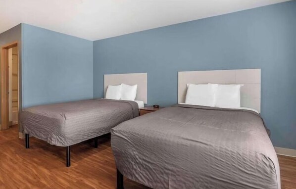 A room with two beds, wooden flooring, and light blue walls.
