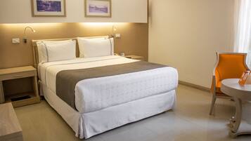Quarto de hotel com uma cama grande, mesas de cabeceira, uma cadeira e uma pequena mesa.