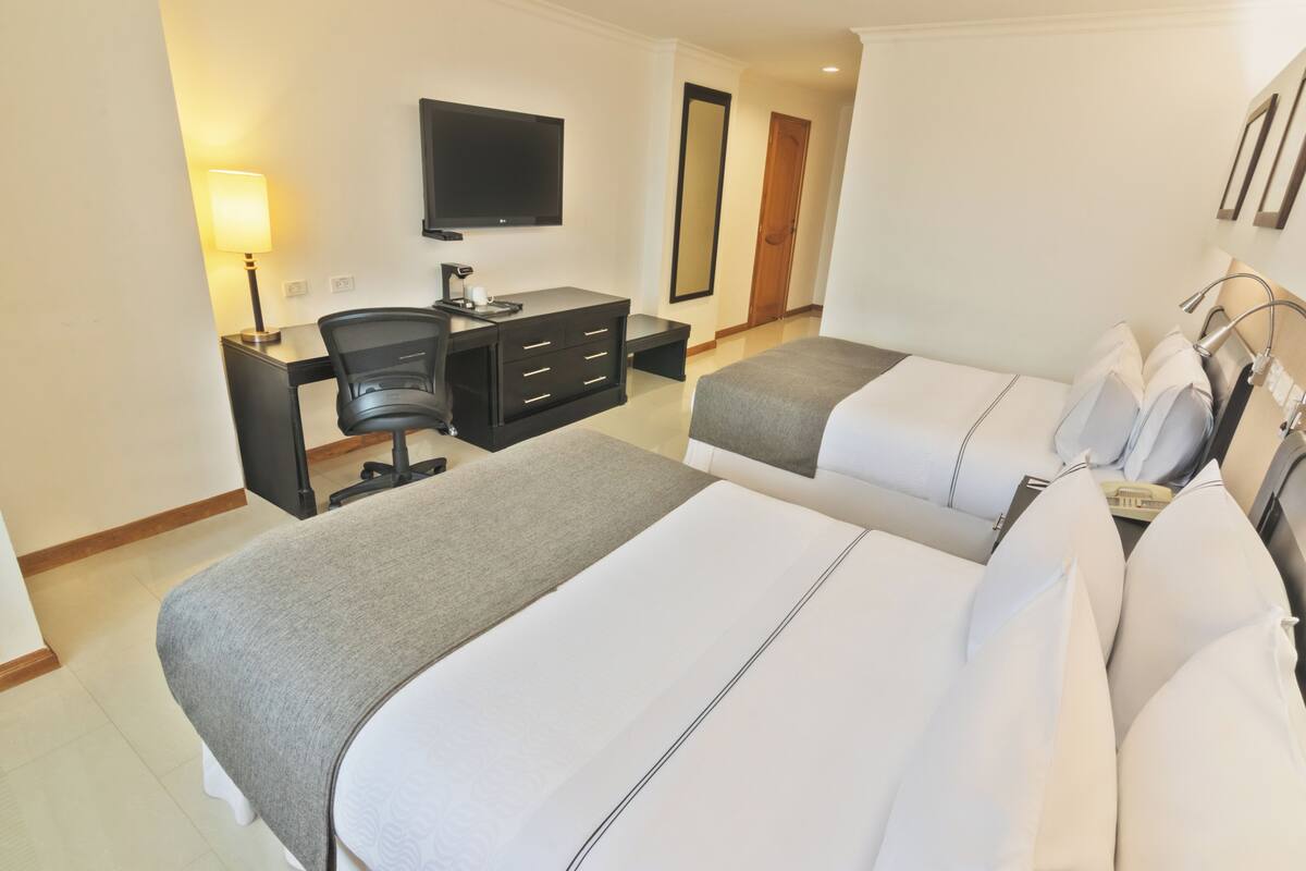 A hotel room with two beds, a desk with a chair, a TV, and a mirror.