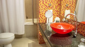A bathroom with a red sink, a white toilet, and a shower area.