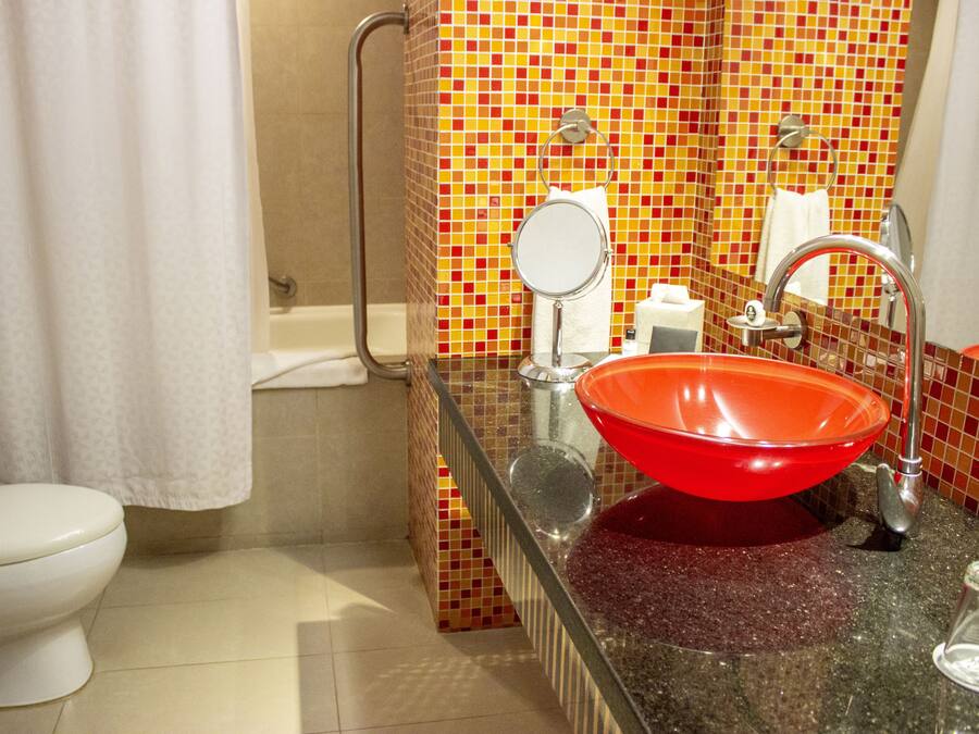A bathroom with a red sink, a white toilet, and a shower area.