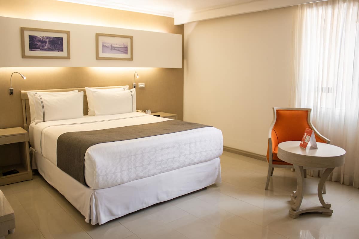 A hotel room with a bed, bedside tables, a chair, and a small table.
