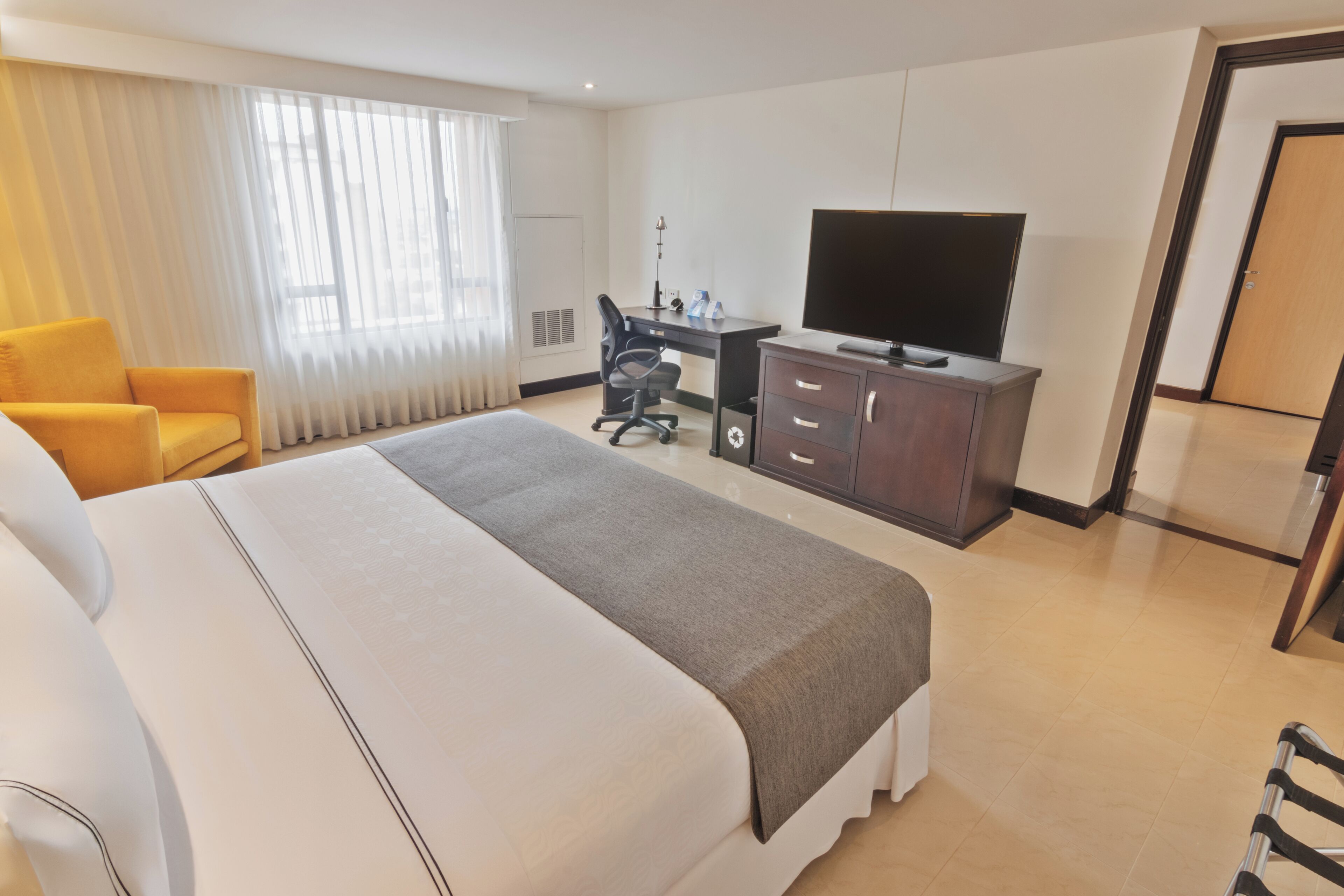 Habitación de hotel con una cama grande, un escritorio con silla, un televisor y un armario.