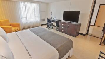 Habitación de hotel con una cama grande, un escritorio con silla, un televisor y un armario.