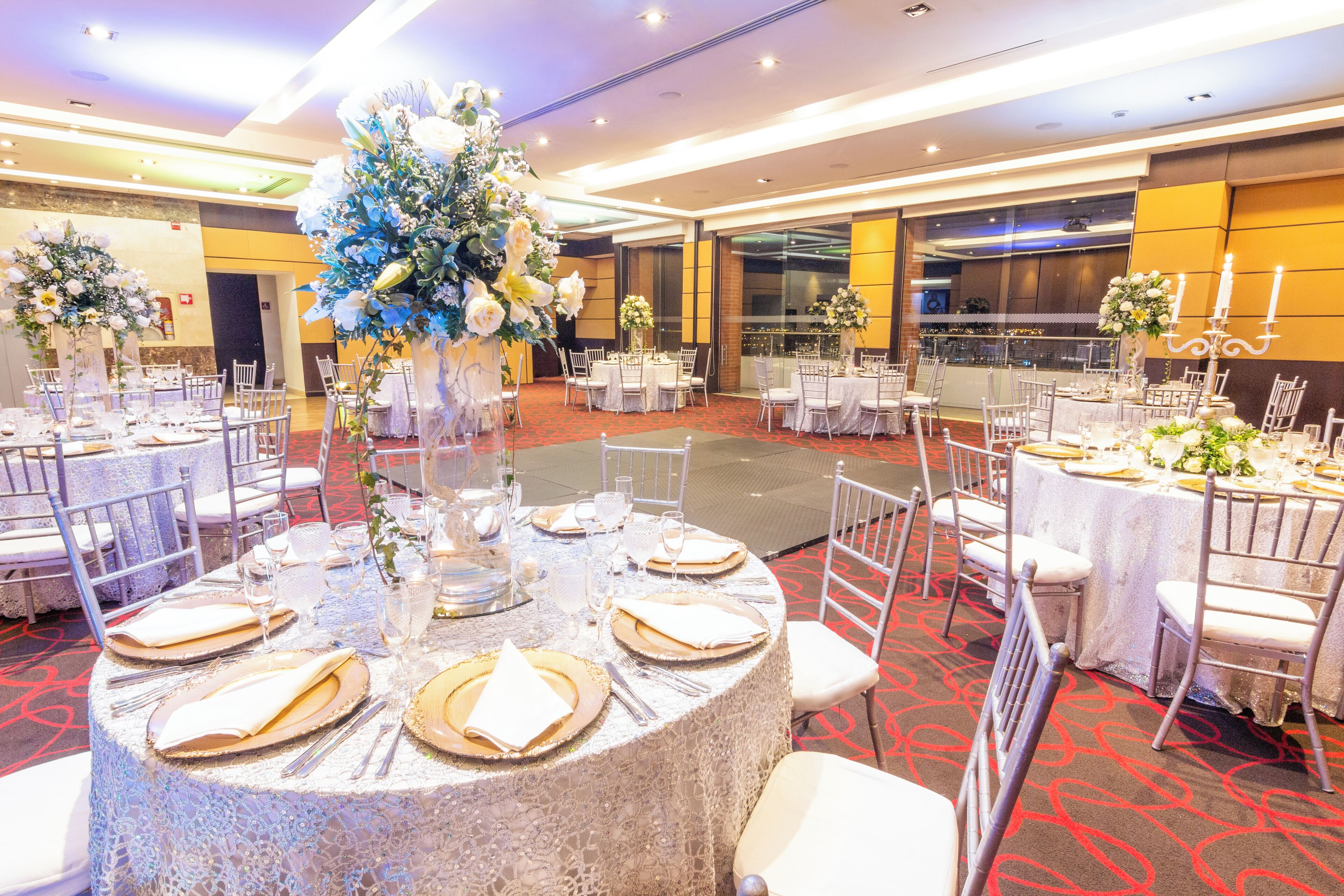 A banquet hall with round tables set for dining, surrounded by white chairs.