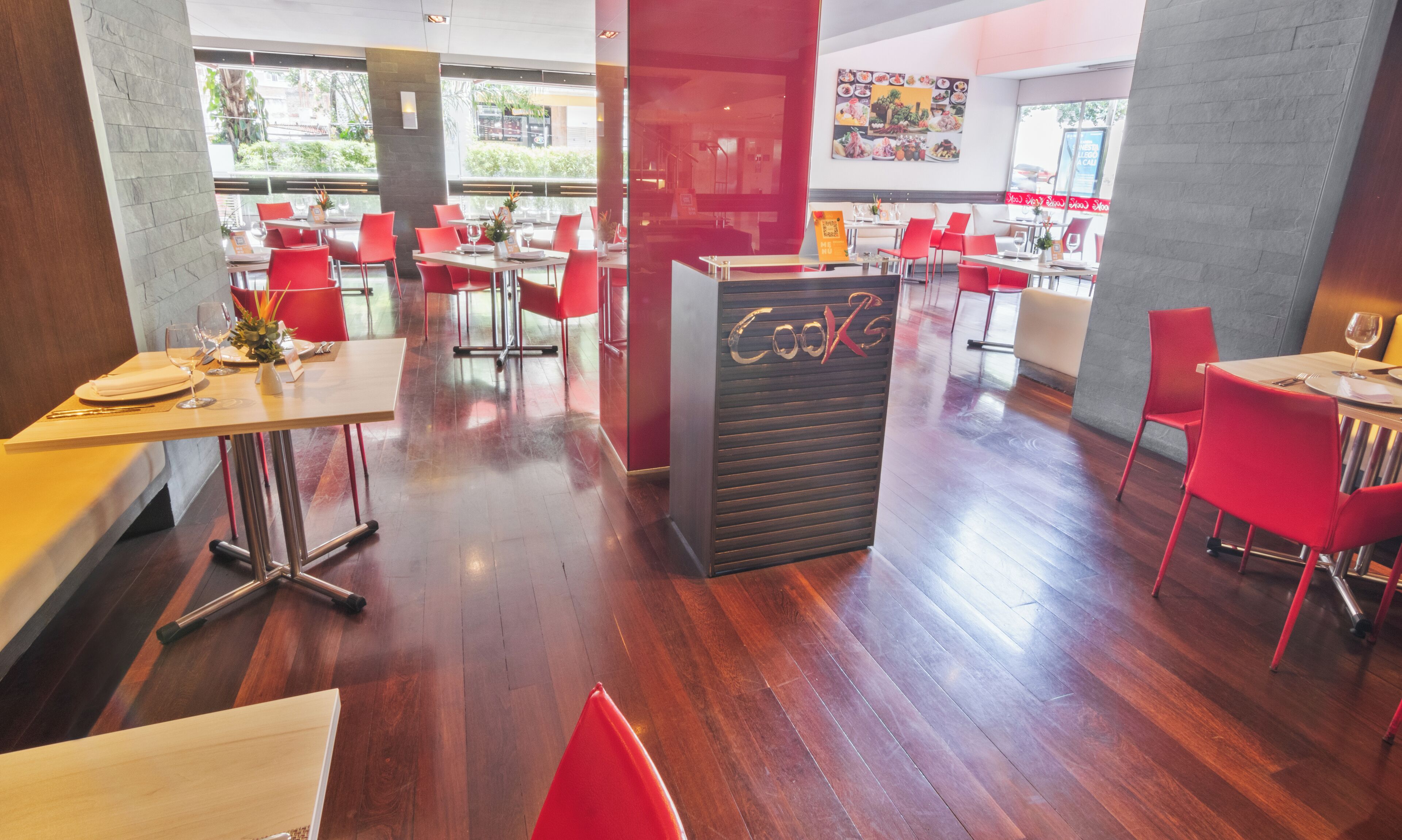 A restaurant interior with wooden floors, red chairs, and tables set for dining.