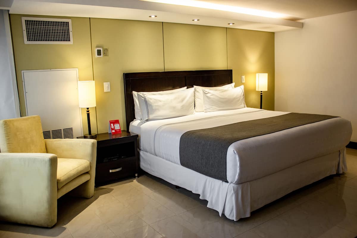 A hotel room with a large bed, bedside lamps, a chair, and a nightstand.
