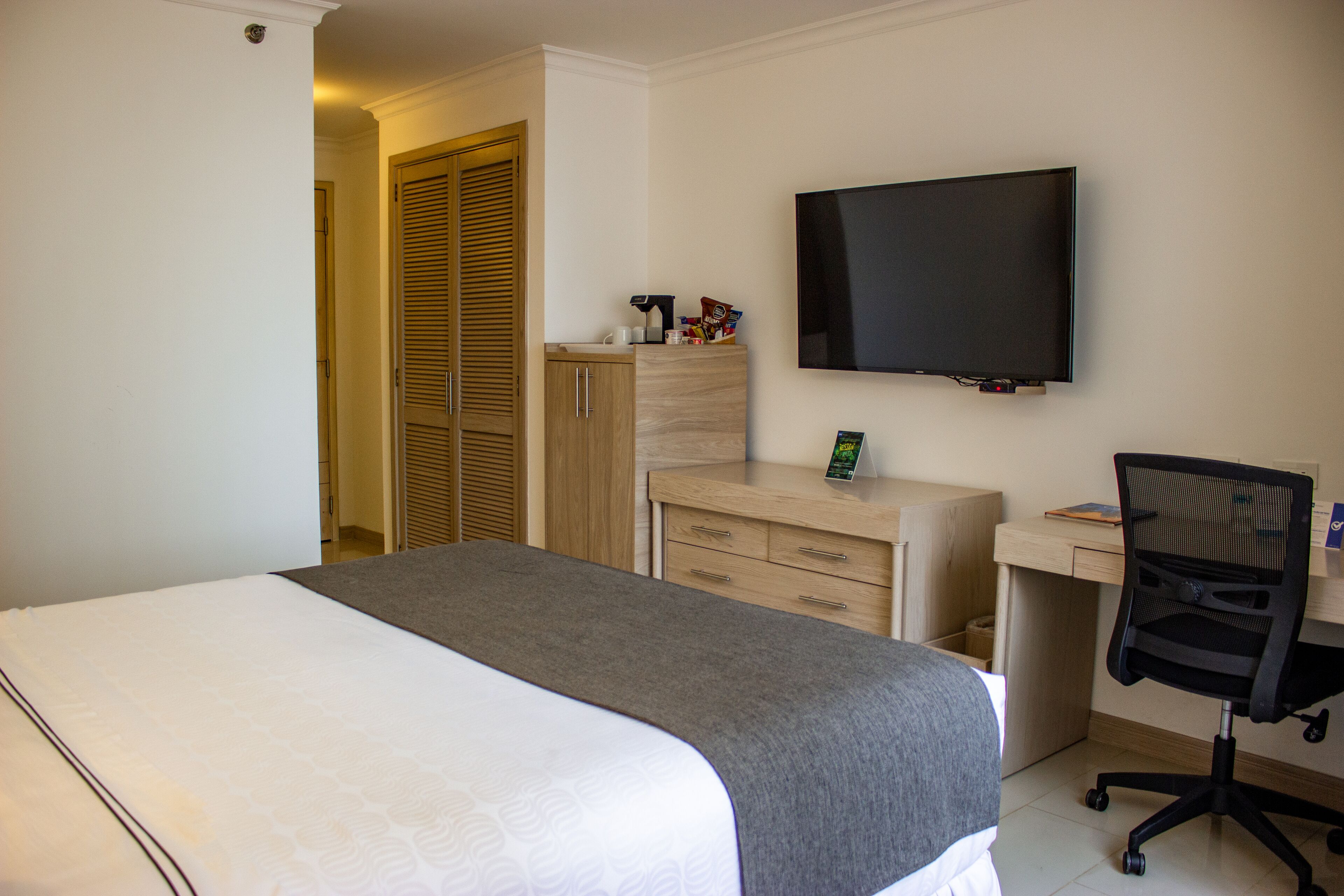 Habitación de hotel con cama, escritorio, silla, televisión y armario.