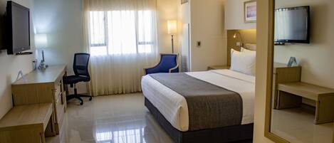 A hotel room with a bed, desk, chair, and a television.