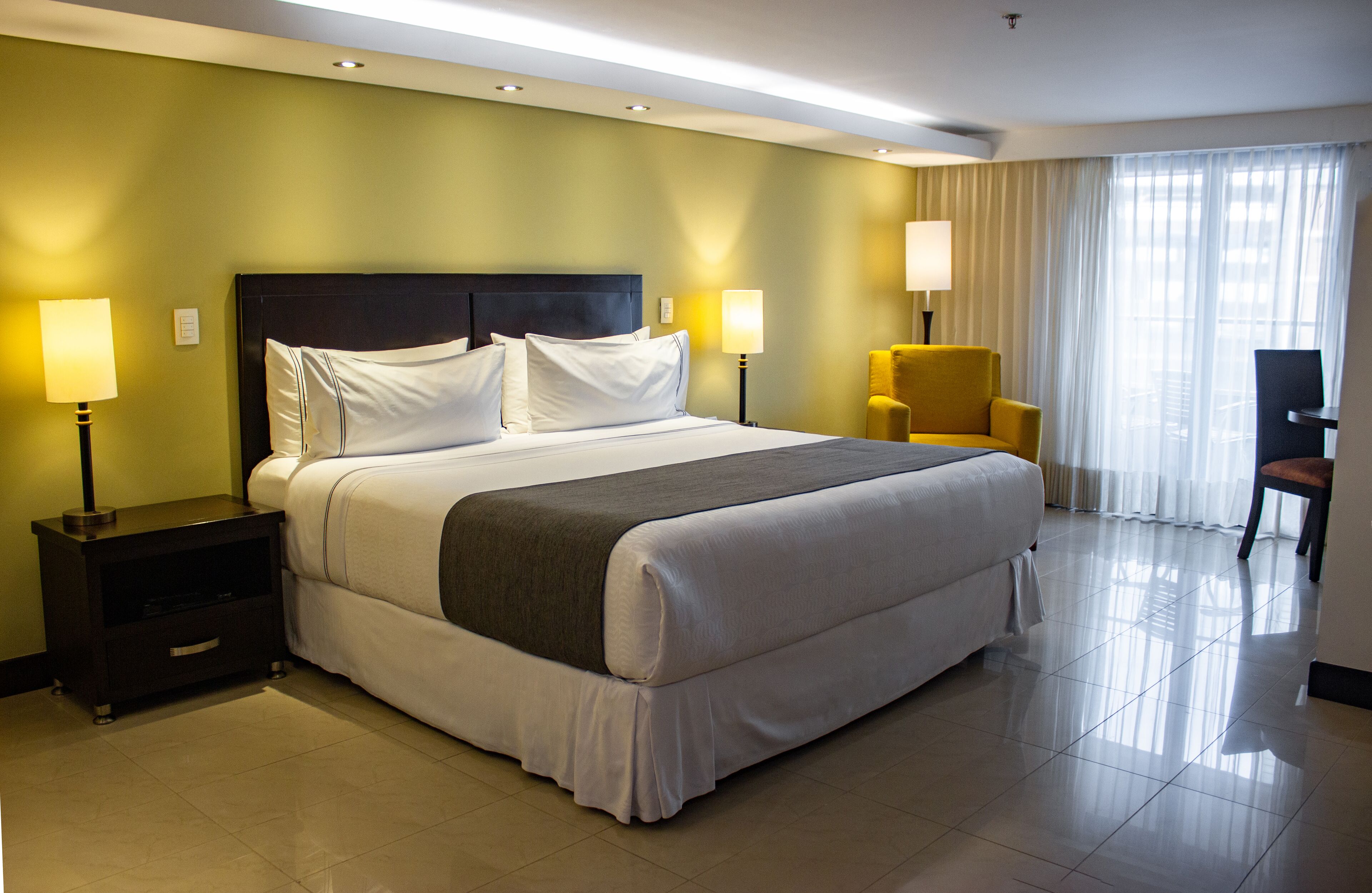 Una habitación de hotel con una cama grande, dos lámparas de noche, una silla y un escritorio.
