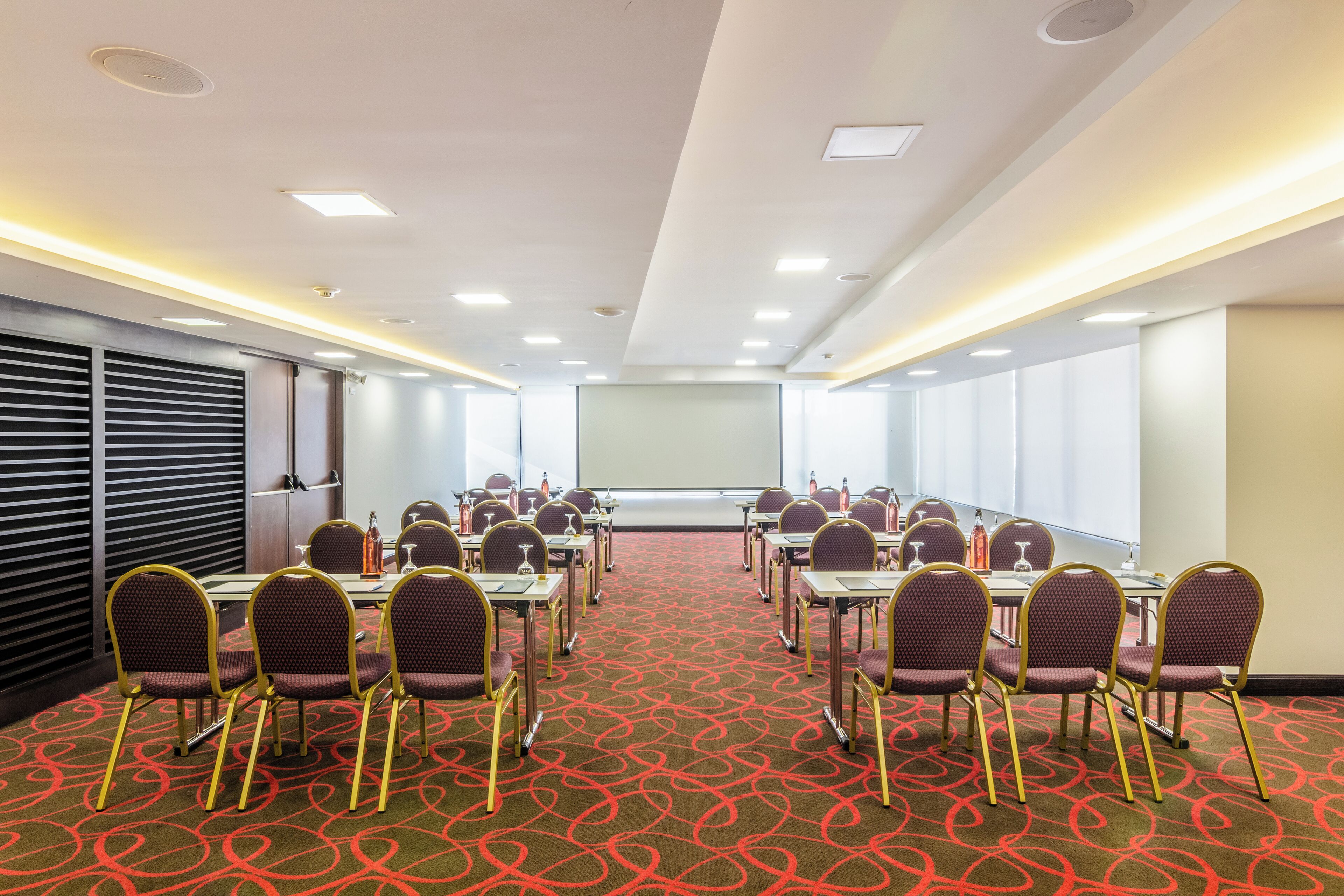 Une salle de conférence dotée d’un tapis rouge, de plusieurs tables, de chaises et d’un écran de projection.