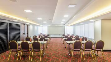 A conference room with a red carpet, multiple tables, chairs, and a projector screen.