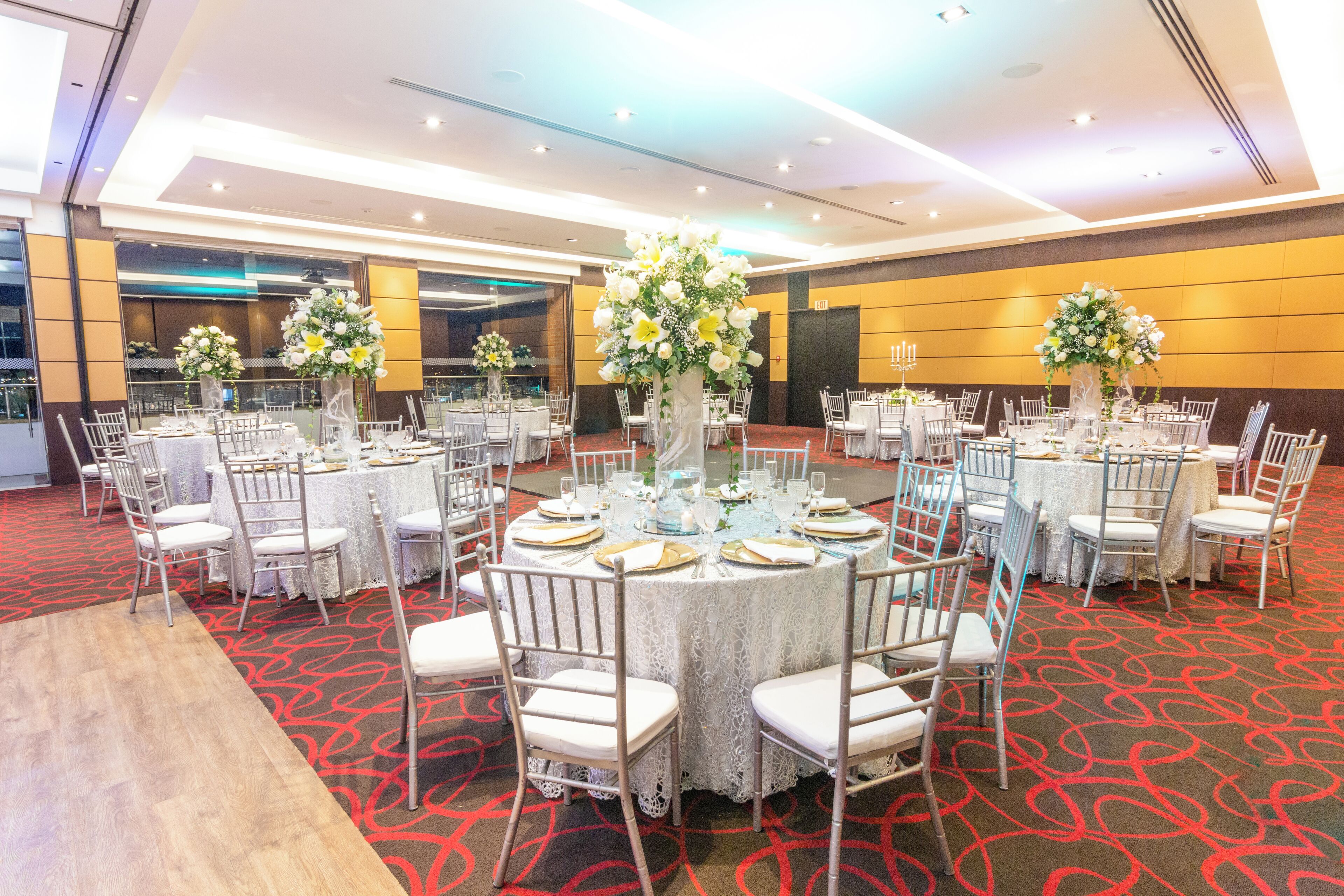 A banquet hall with round tables set for events, featuring white tablecloths and floral centerpieces.