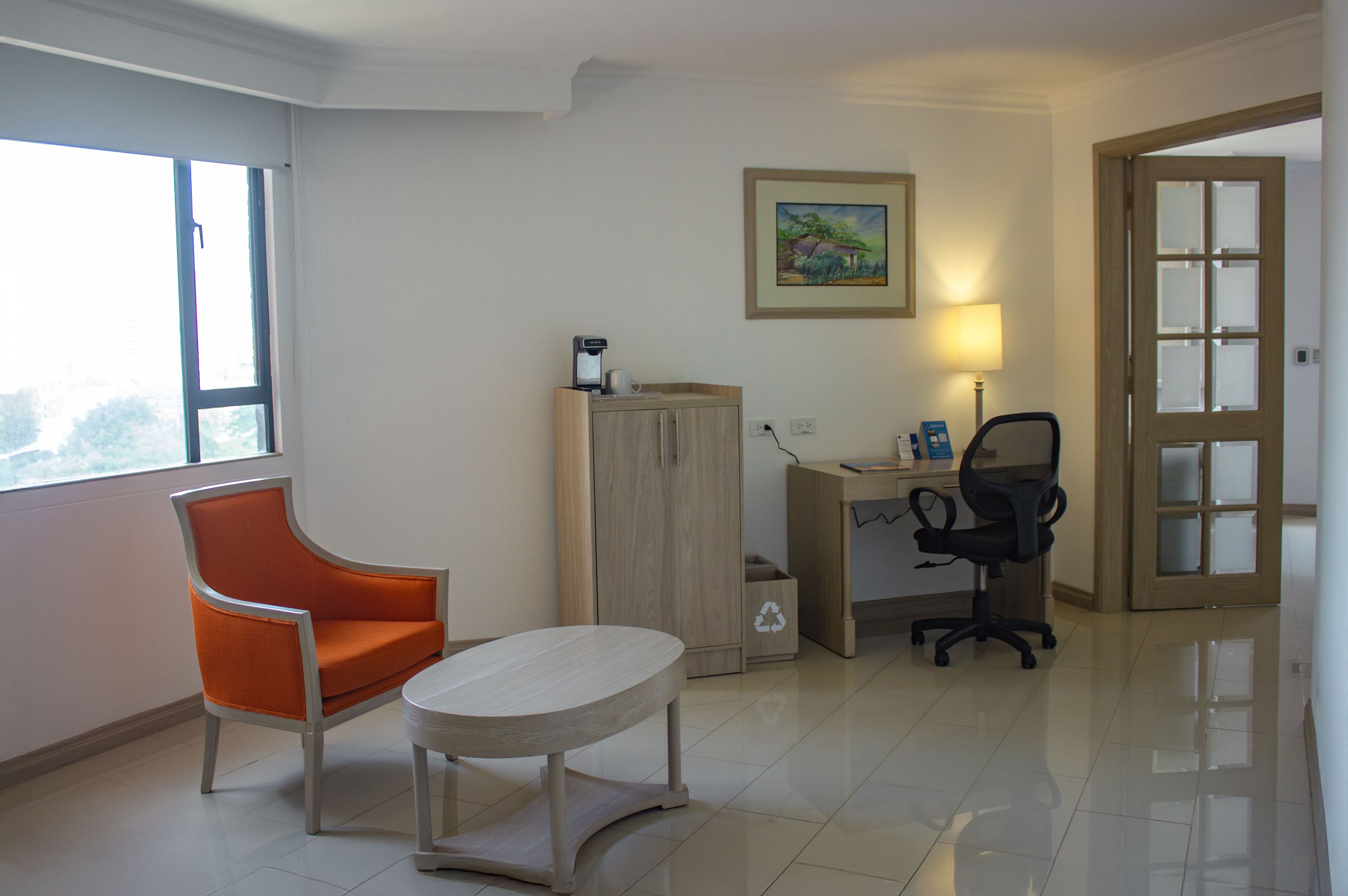 A room with a window, a desk with a chair, a small table, and a cabinet.