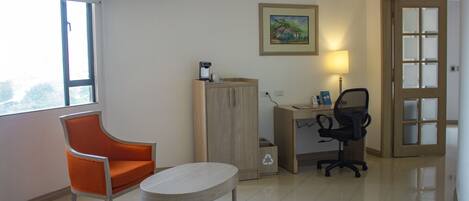 A room with a window, a desk with a chair, a small table, and a cabinet.
