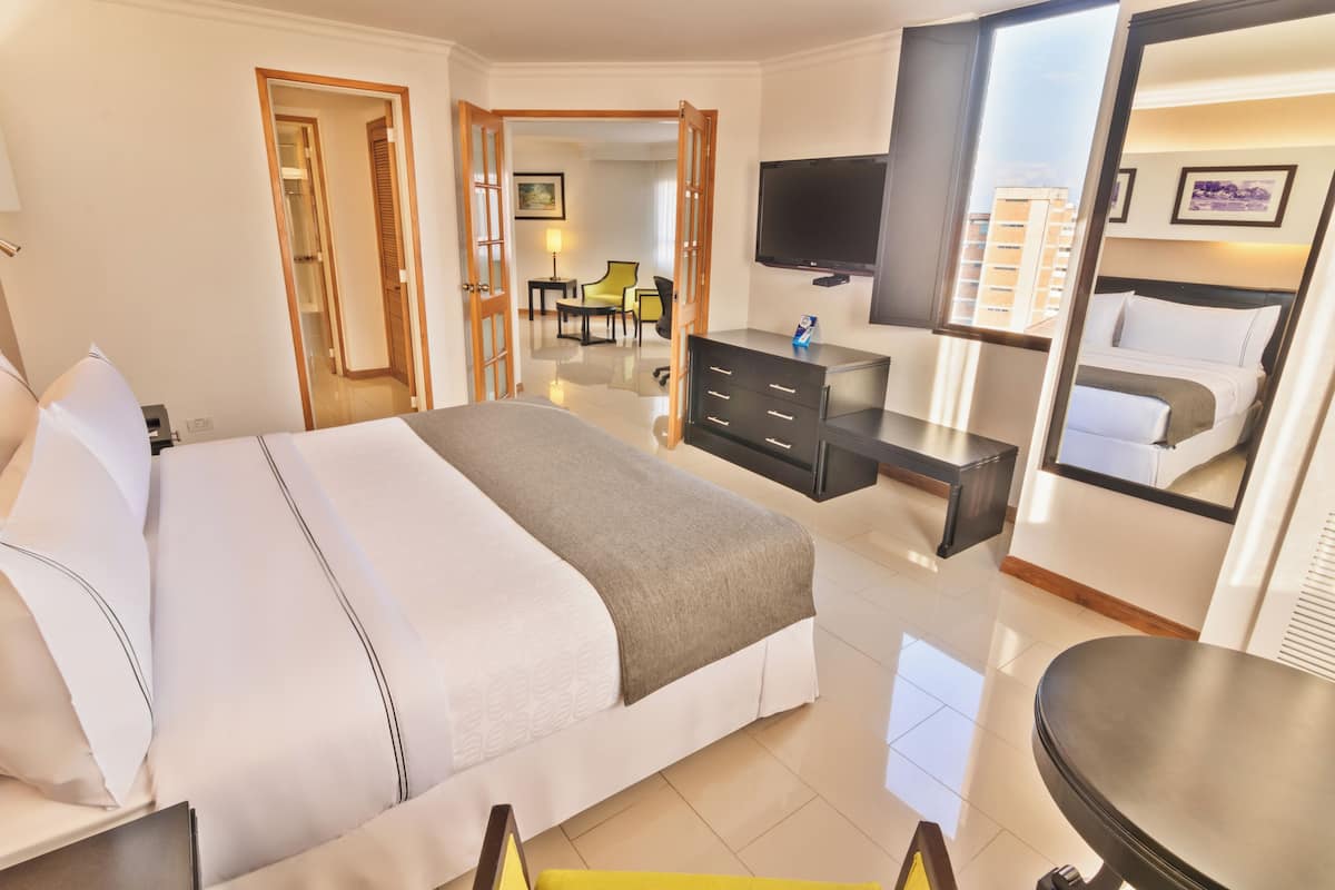 A hotel room with a bed, a desk, a chair, a TV, and a bathroom mirror.