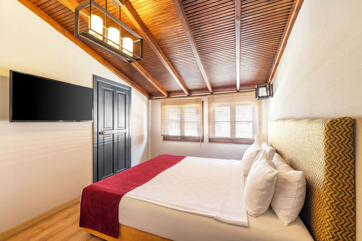 A bedroom with a bed, a television mounted on the wall, a door, and windows with blinds.