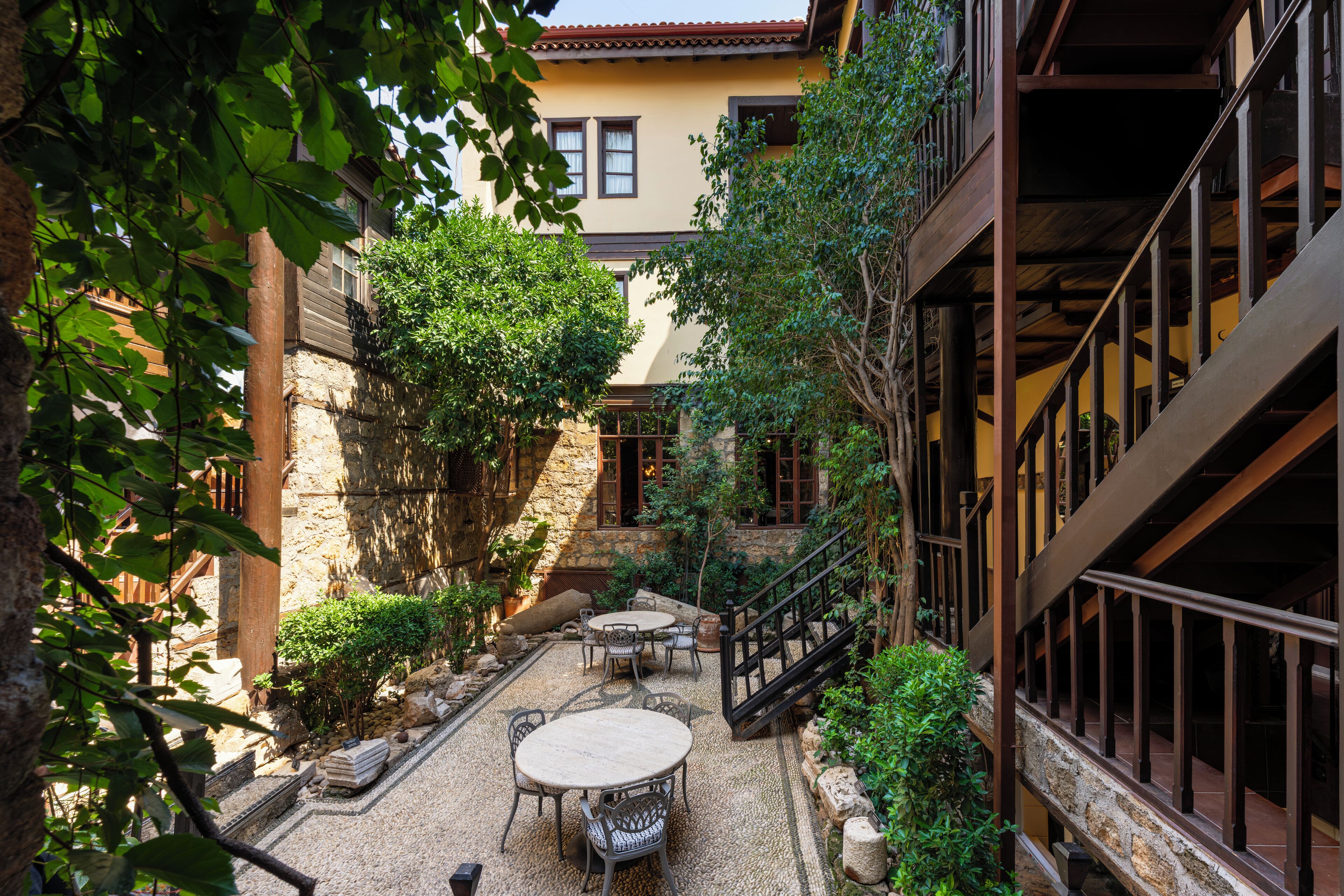 A courtyard with stone flooring, a wooden staircase, and a seating area with tables and chairs.