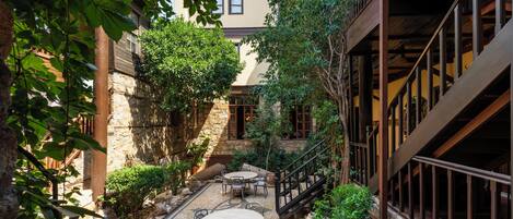 A courtyard with stone flooring, a wooden staircase, and a seating area with tables and chairs.