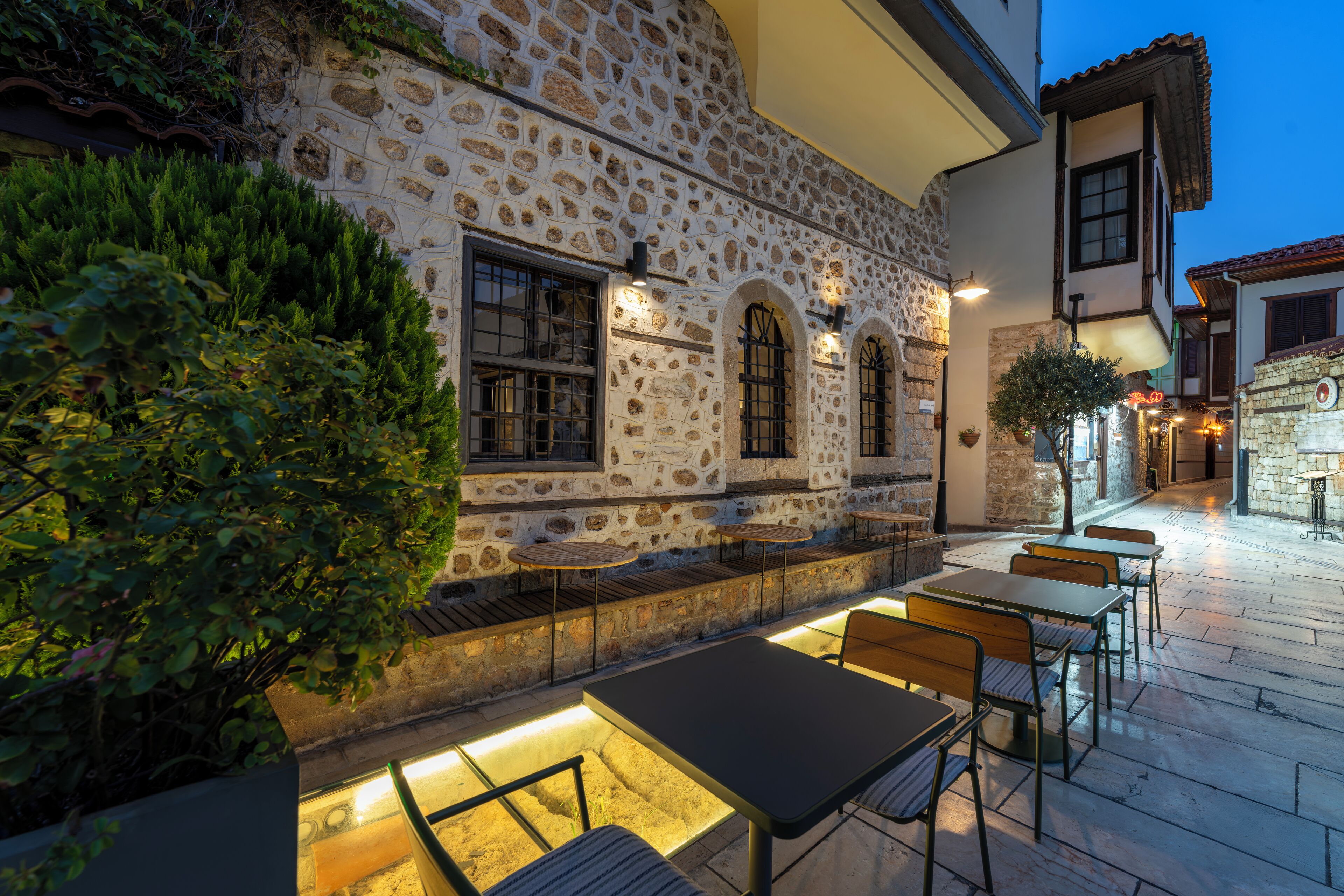 An outdoor seating area with stone walls and tables, surrounded by greenery.