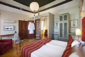 Classic hotel room with a large bed, wardrobe, desk, and television.