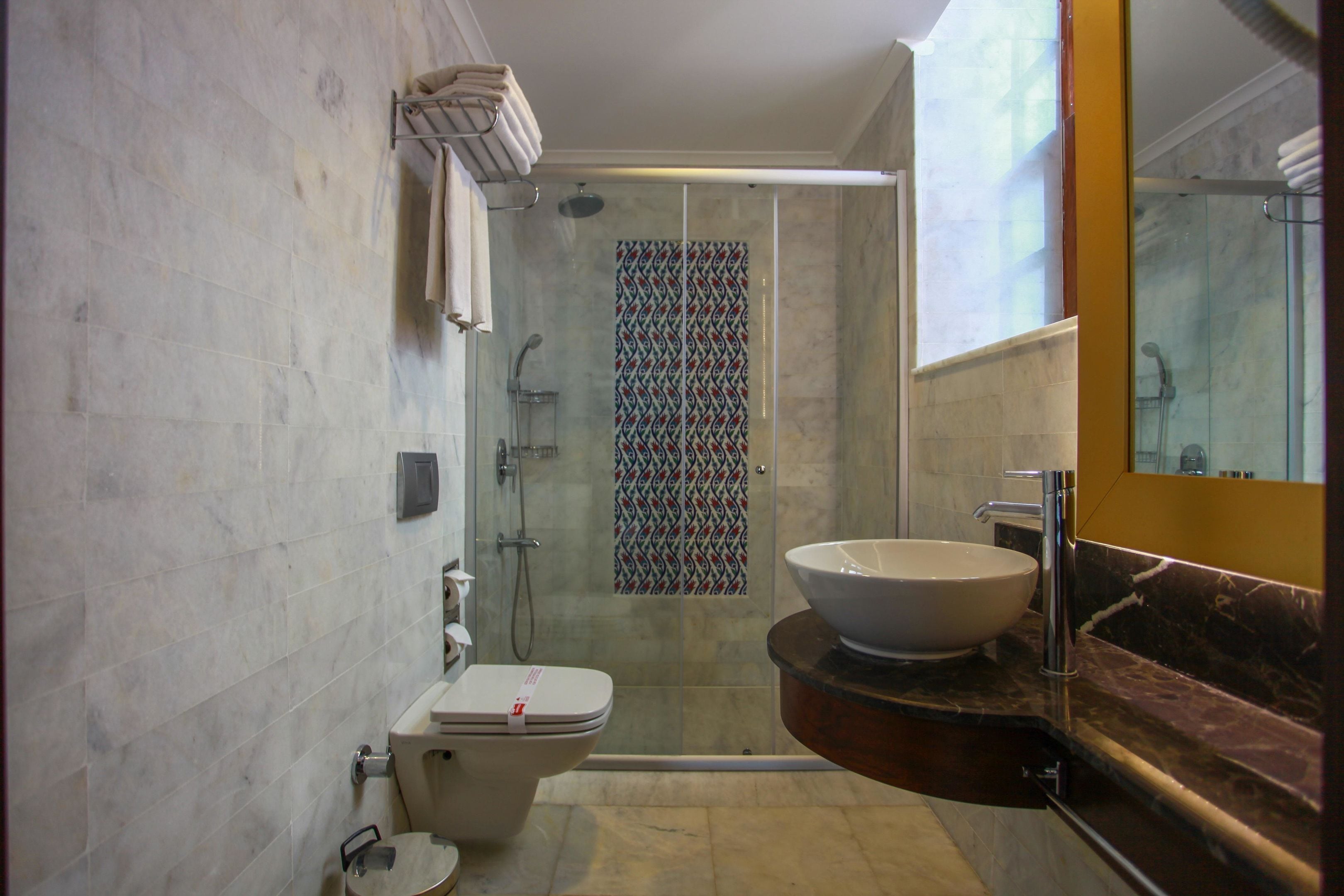 A modern bathroom with a glass-enclosed shower, a white toilet, and a marble countertop with a large sink.