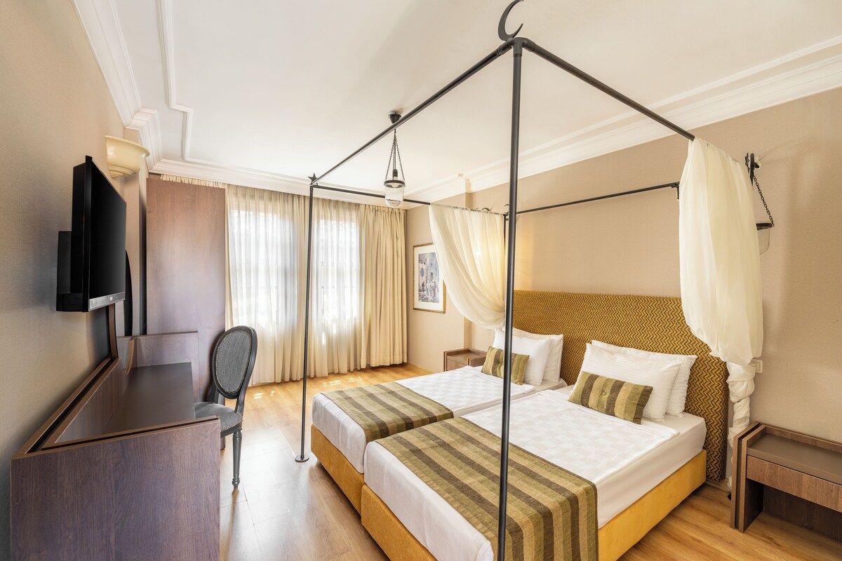 Une chambre d’hôtel avec un lit à baldaquin, un bureau et une télévision.