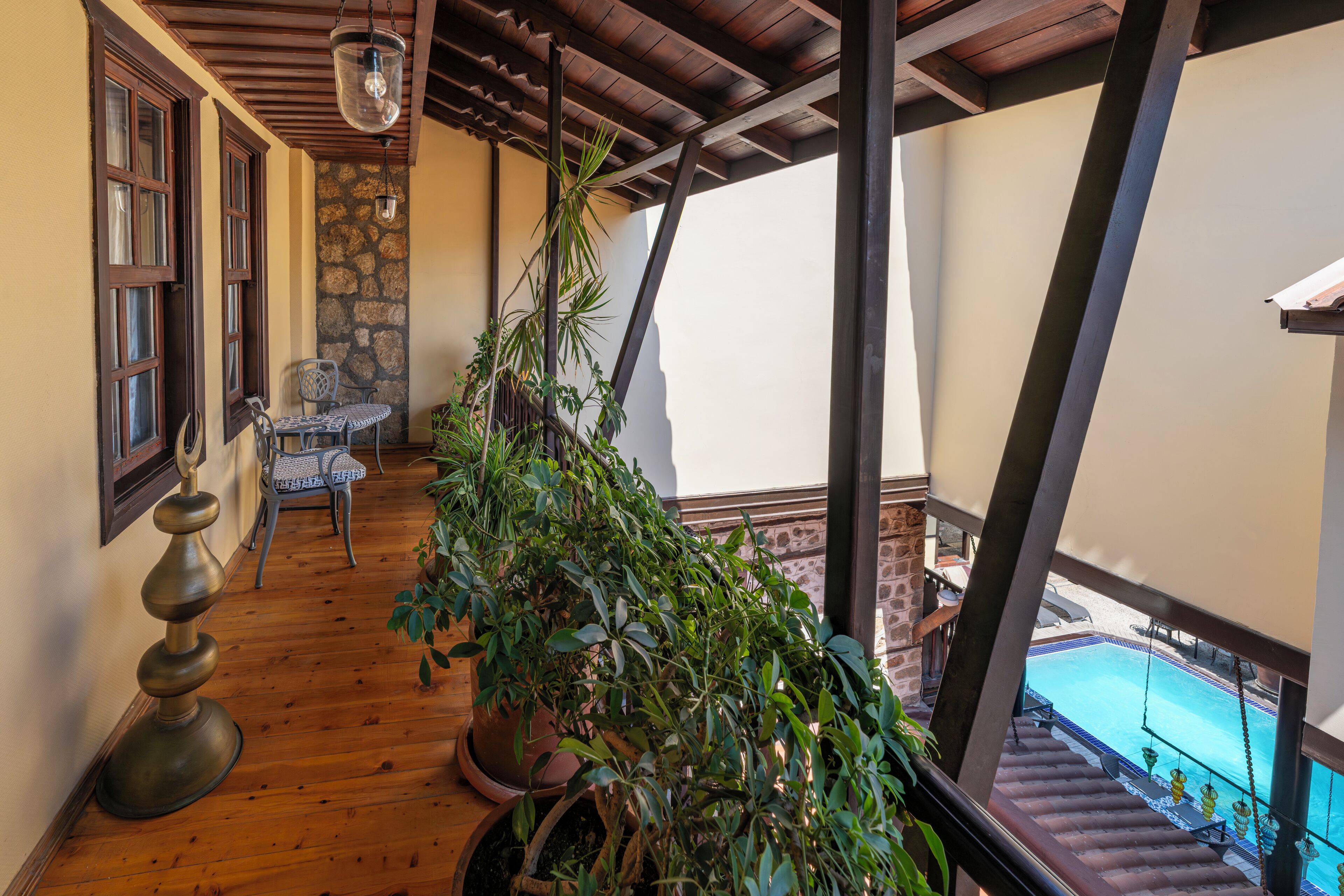 A balcony with wooden flooring, a table and chair, potted plants, and a view of a swimming pool.