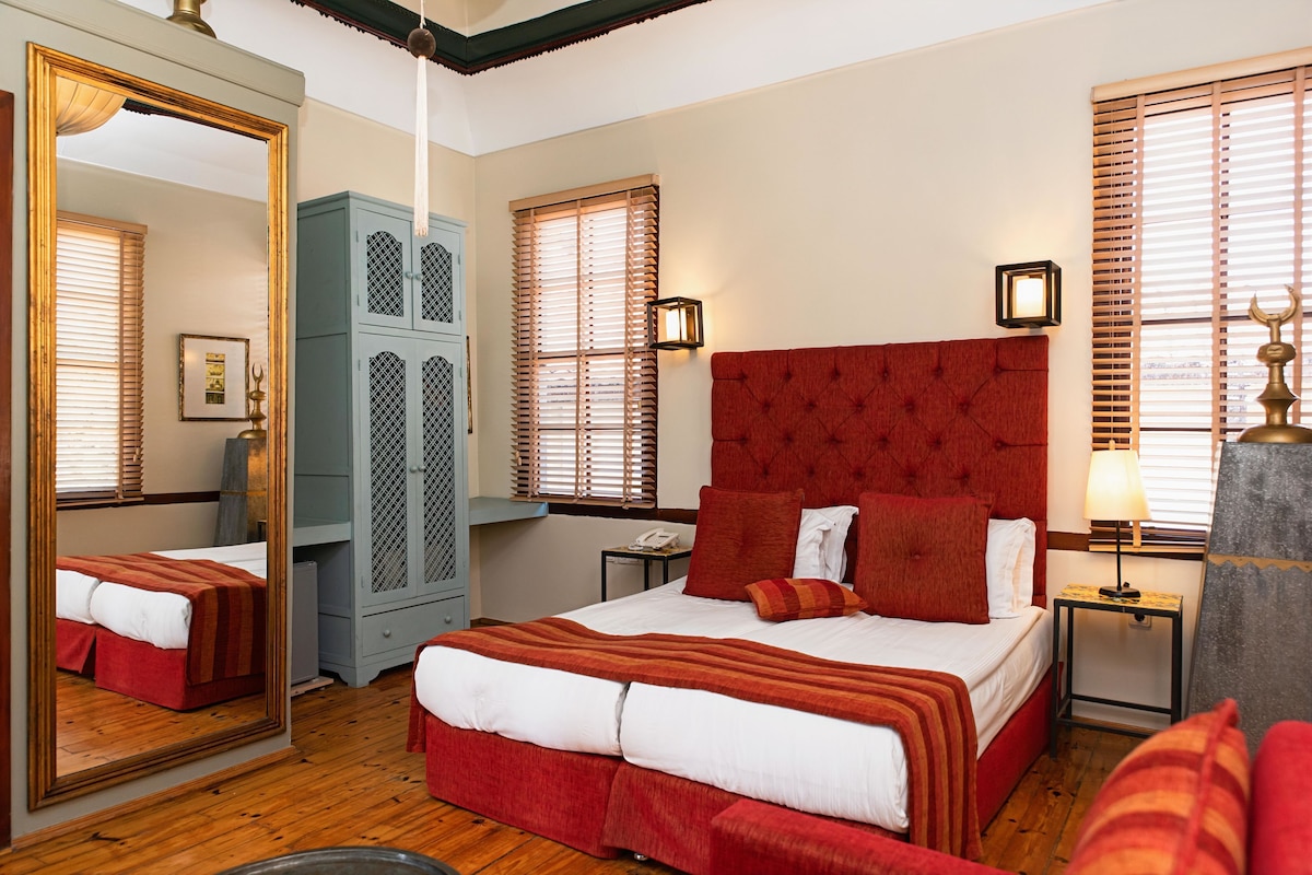 Habitación de hotel con una cama grande, un armario, un espejo y una mesita de noche con una lámpara.