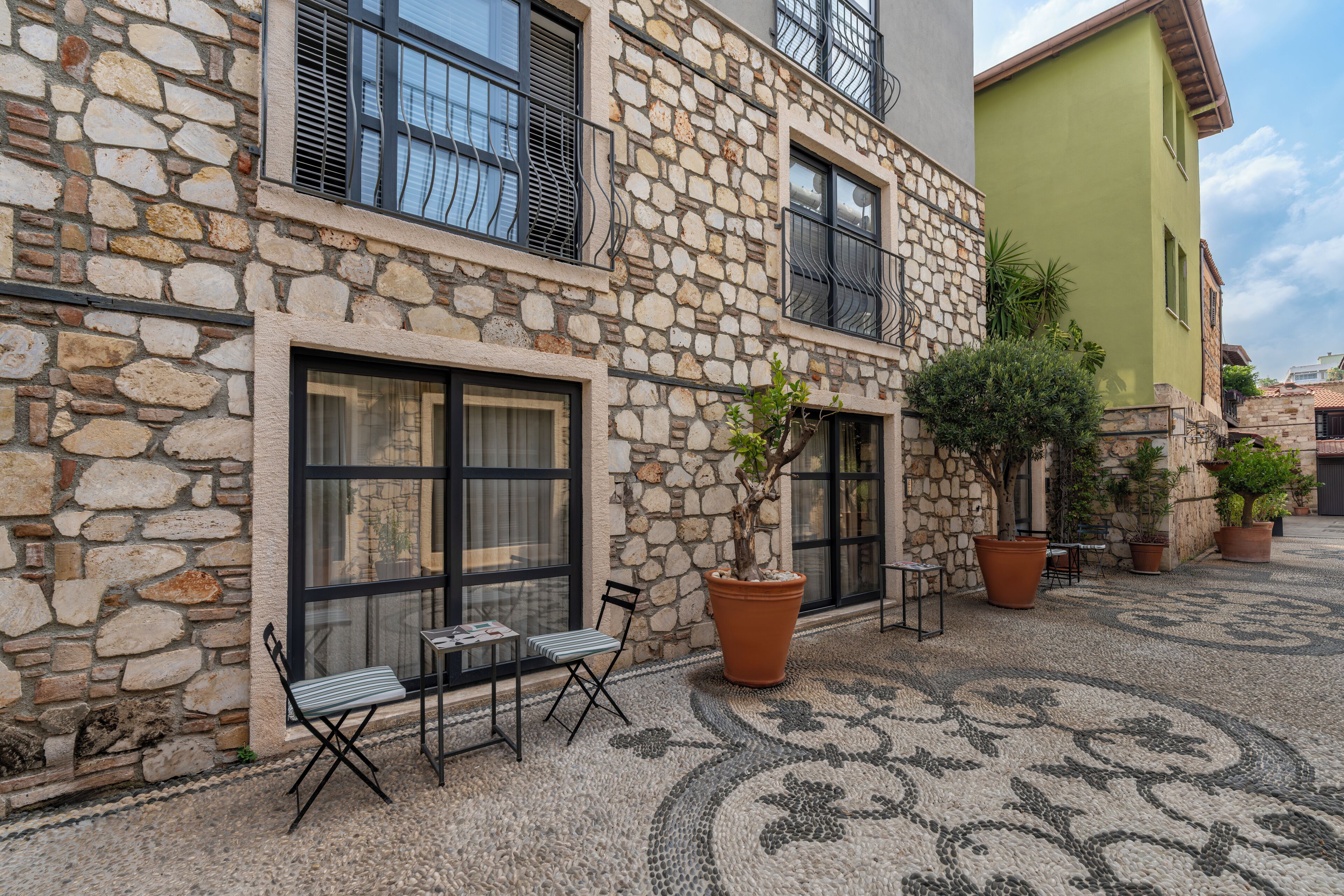 Un edificio de piedra con patio de baldosas, mobiliario exterior y plantas en macetas.