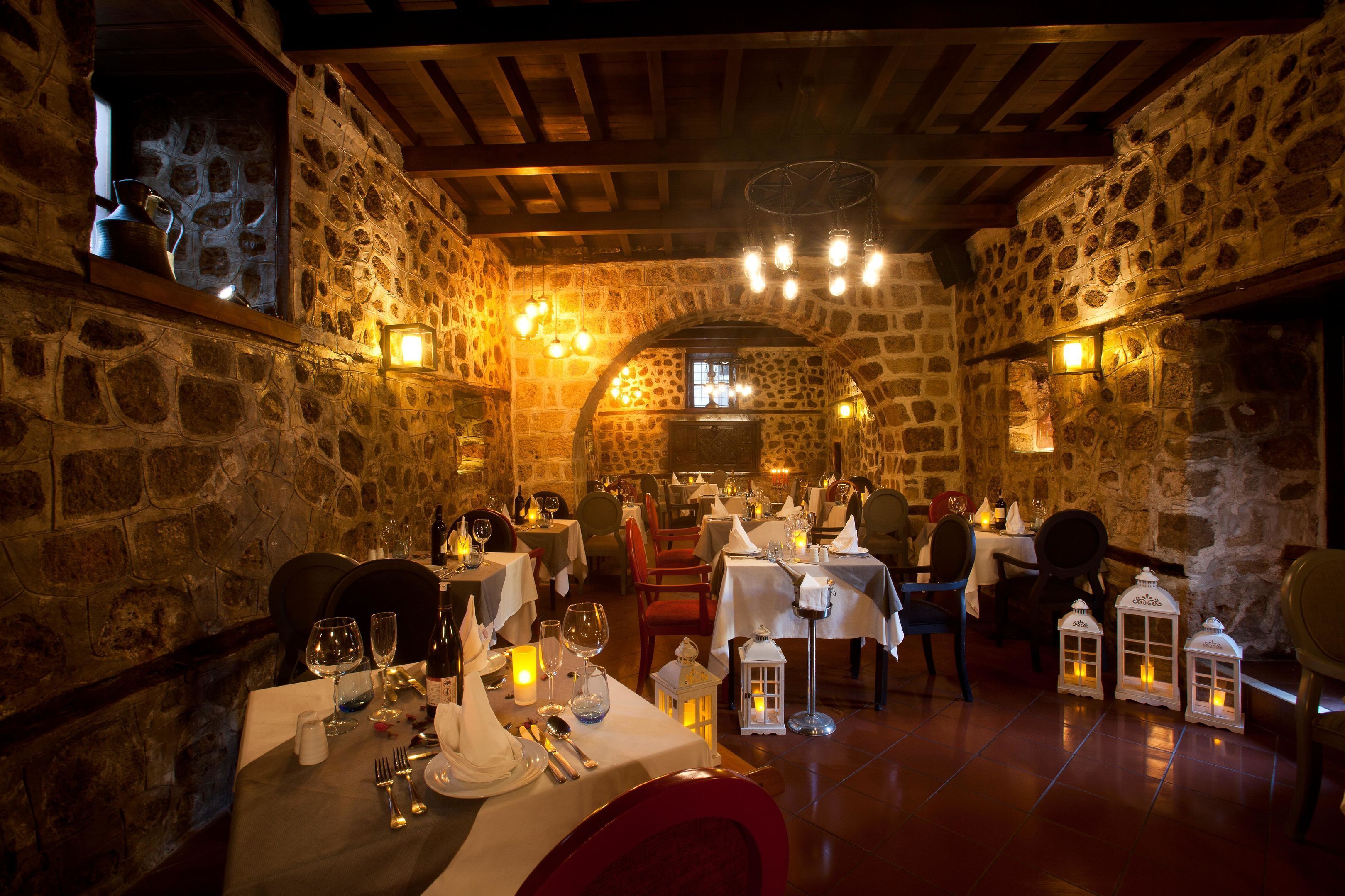 Ein Restaurant mit Stehwänden und Holzbalken, Tische gedeckt mit weißen Tischdecken und Kerzen, sowie Laternen auf dem Boden.