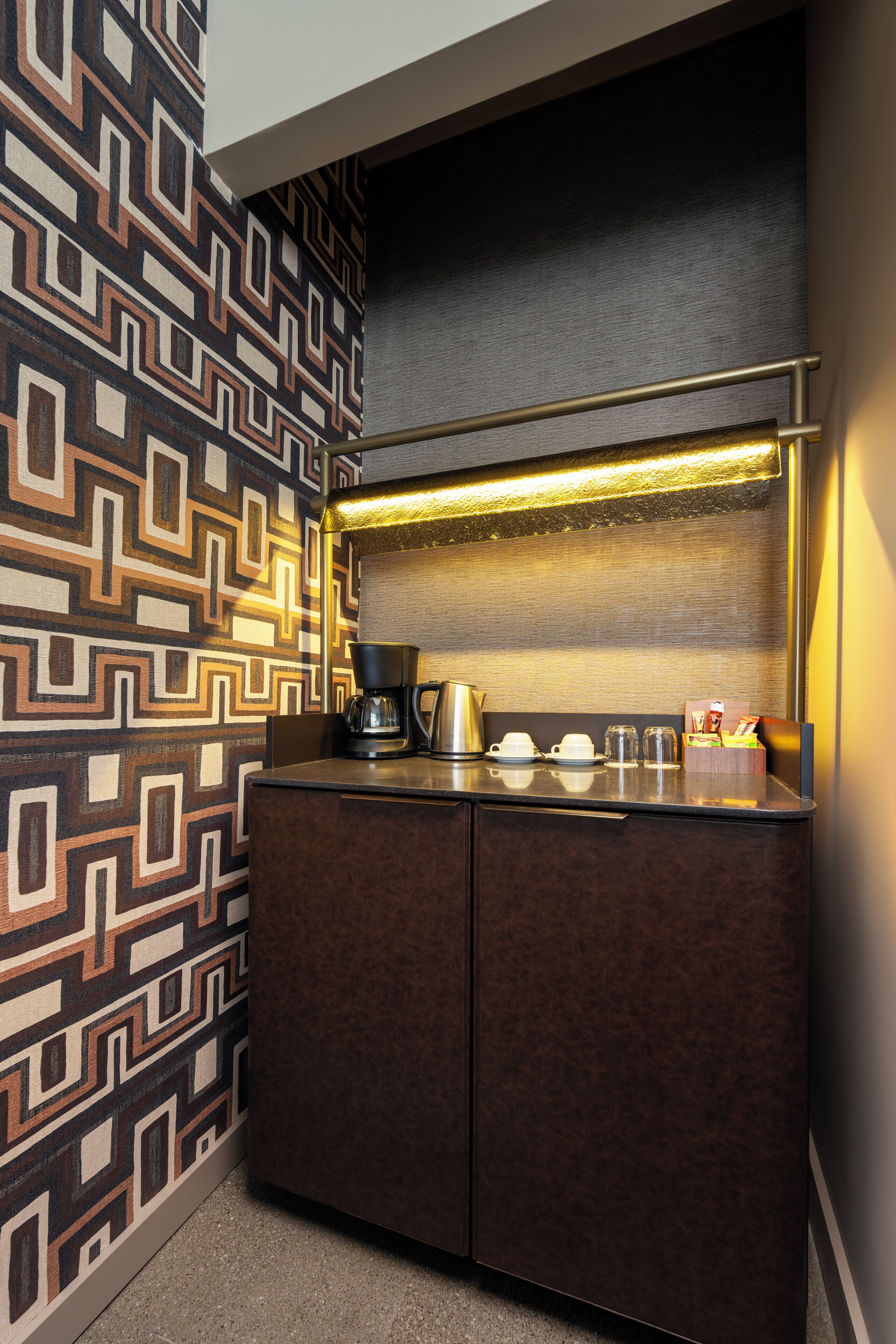 Une petite cuisine équipée avec un mur décoré de motifs, une machine à café, des tasses et un petit comptoir pour prendre le petit-déjeuner.
