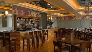 A bar area with wooden bar stools, a counter with bottles, and a floral wall mural. - The Claremont  (Douglas)