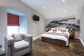 Un dormitorio con cama, una silla, un televisor y un mural de una escena histórica.
