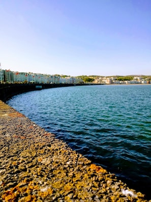 Un paseo marítimo con costa rocosa y una hilera de edificios al fondo.