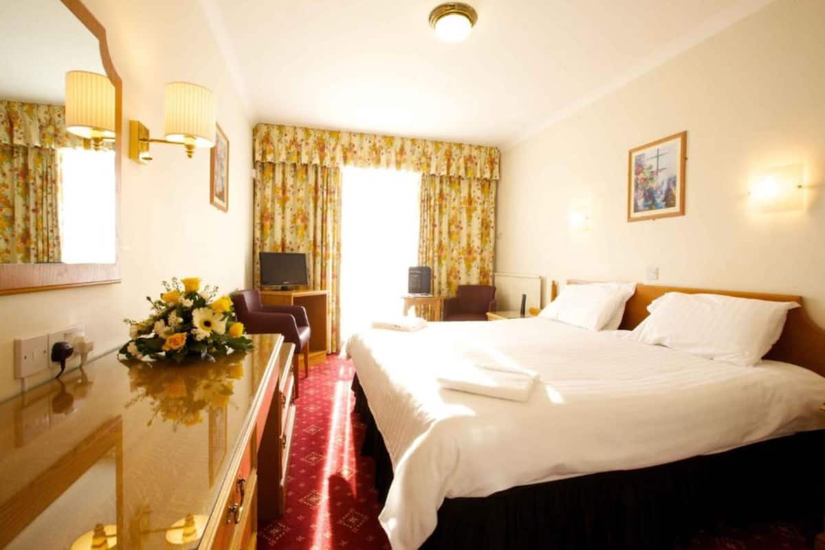 A hotel room with a large bed, a desk with a computer, a TV, and a mirror.