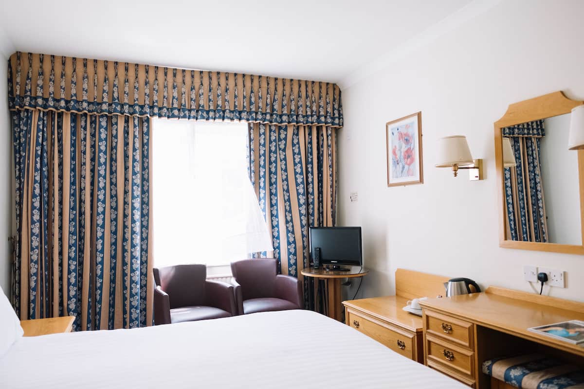A hotel room with a bed, a desk, a chair, a television, and curtains.