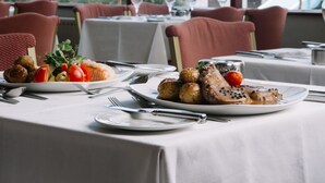 A restaurant table set with plates of food, including roasted meat and vegetables, and a wine glass. - Apollo Jersey (St. Helier)