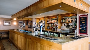 A bar area with wooden paneling, a counter with a cash register, and a menu board. - Apollo Jersey (St. Helier)