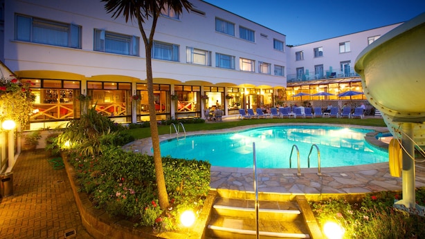 A hotel with a swimming pool, outdoor seating, and a well-lit patio area. - Apollo Jersey (St. Helier)