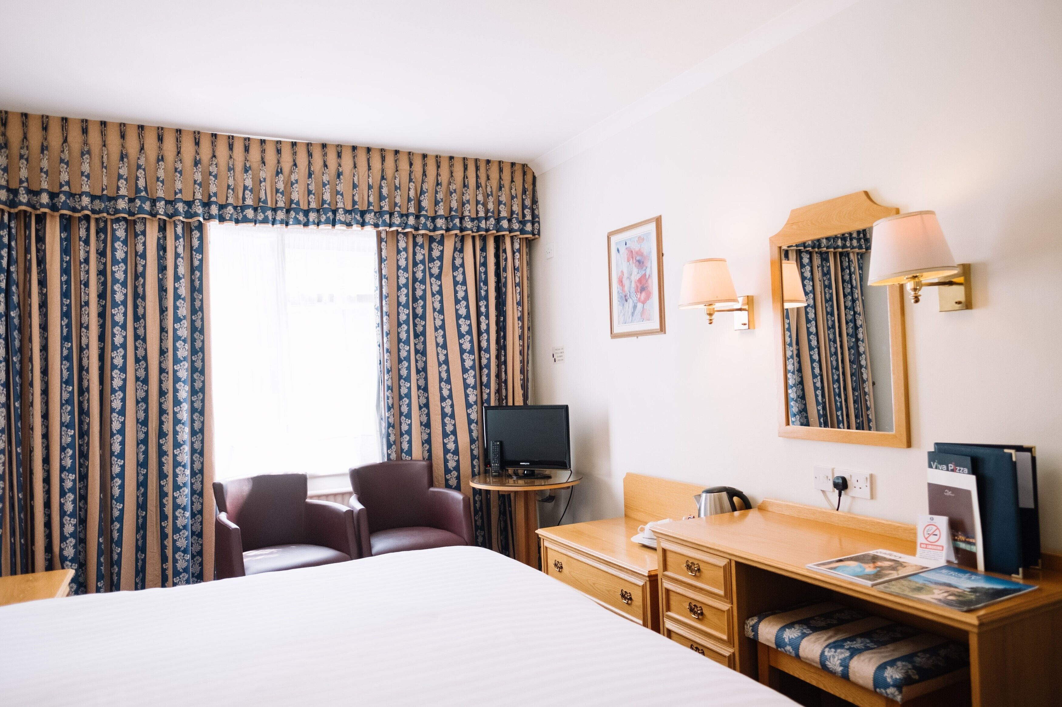 A hotel room with a bed, a desk, a chair, a television, and a desk lamp.