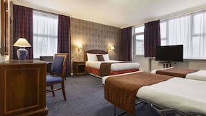 Une chambre d’hôtel avec deux lits, un bureau, une chaise, une télévision et deux lampes fixées au mur.